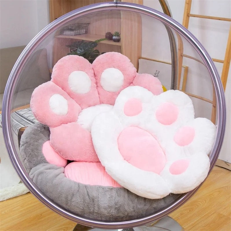 A big grey cat paw cushion where upon it small size white and pink is held upon on a swing