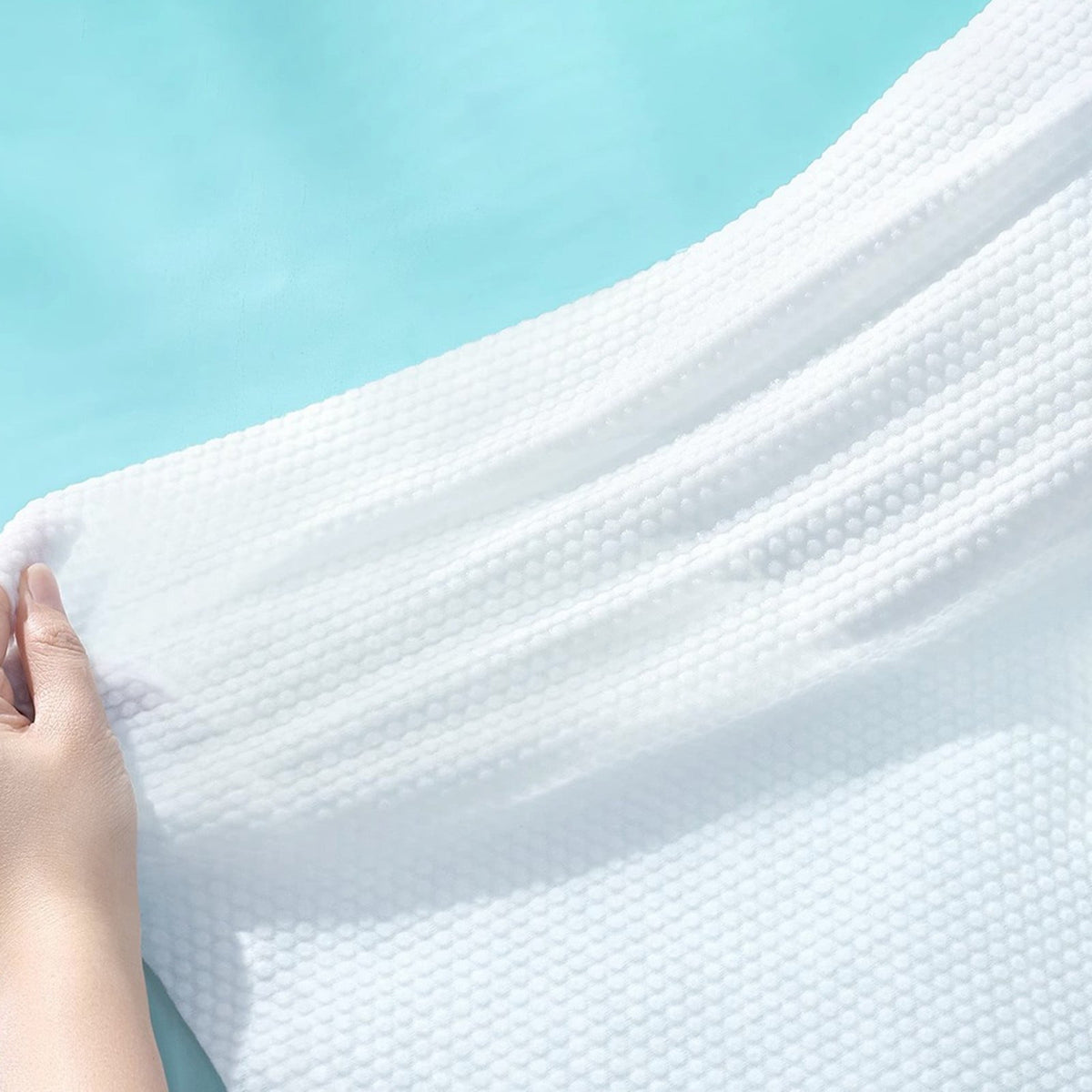 A close-up of a compression bath towel being held by a hand against a light aqua background.