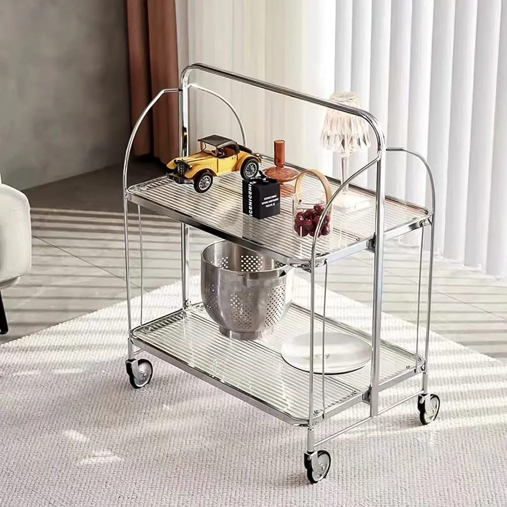  folding 2-tier serving trolley with a chrome finish, glass shelves, and rolling wheels arranged with decor items.