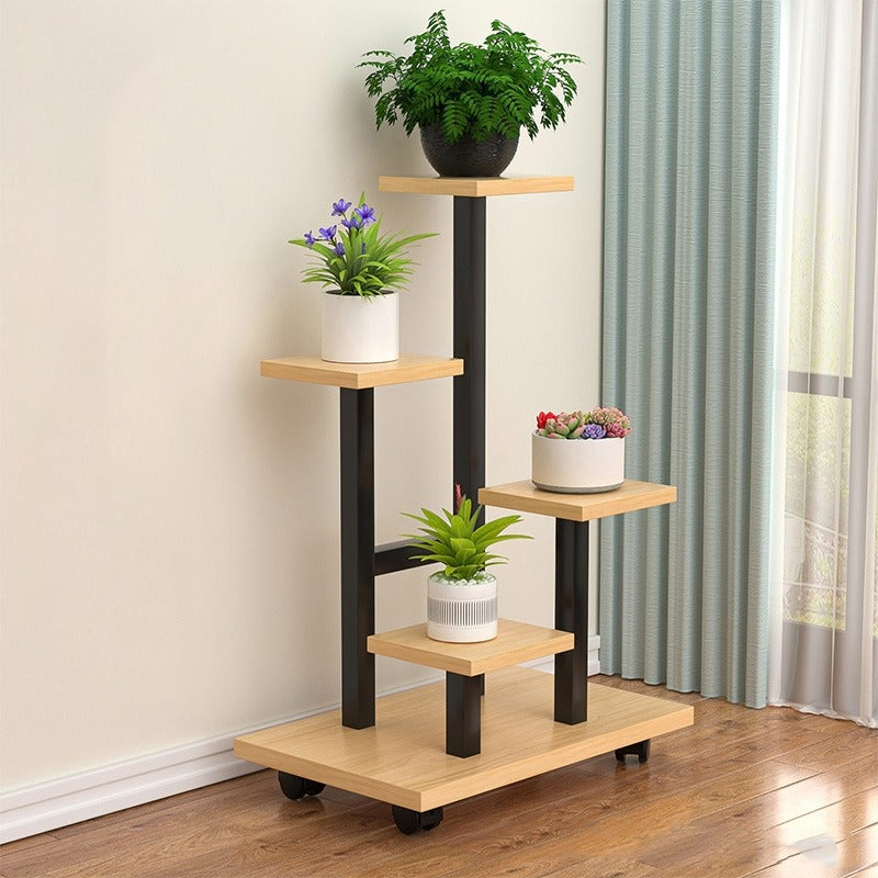 multi-tier indoor plant stand with four staggered shelves displaying different potted plants, placed on wooden flooring beside a window with curtains