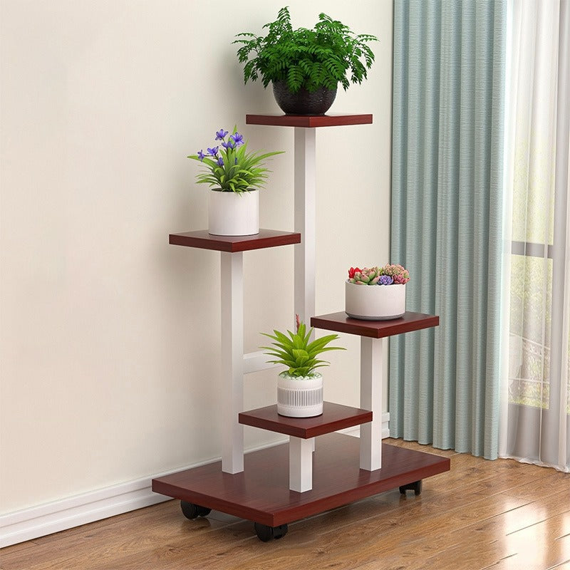 multi-tier indoor plant stand with four staggered shelves displaying different potted plants, placed on wooden flooring beside a window with curtains