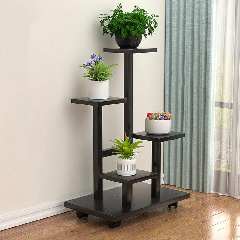 multi-tier indoor plant stand with four staggered shelves displaying different potted plants, placed on wooden flooring beside a window with curtains