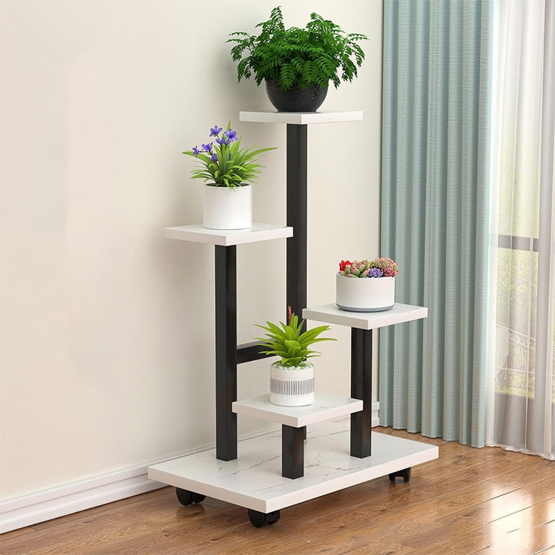 multi-tier indoor plant stand with four staggered shelves displaying different potted plants, placed on wooden flooring beside a window with curtains