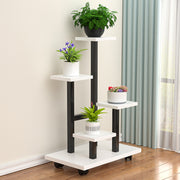 Multi-tier indoor plant stand with four staggered shelves displaying different potted plants, placed on wooden flooring beside a window with curtains.