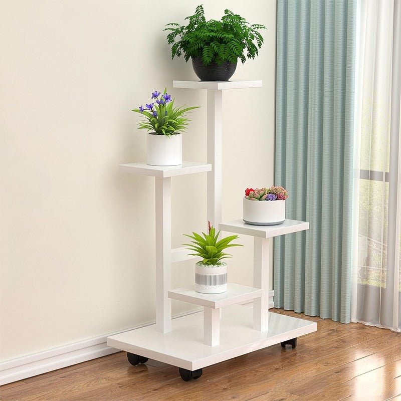 multi-tier indoor plant stand with four staggered shelves displaying different potted plants, placed on wooden flooring beside a window with curtains