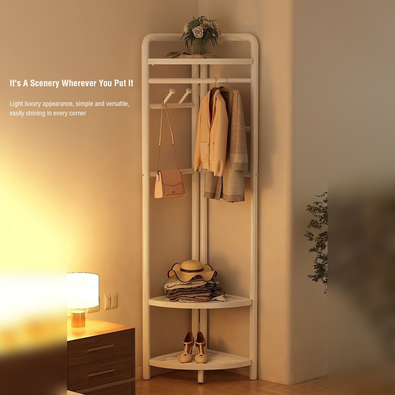White garment rack kept in a corner of bedroom with a plant above, over below comes hanging area where 2 sweaters and a bag is hanged.