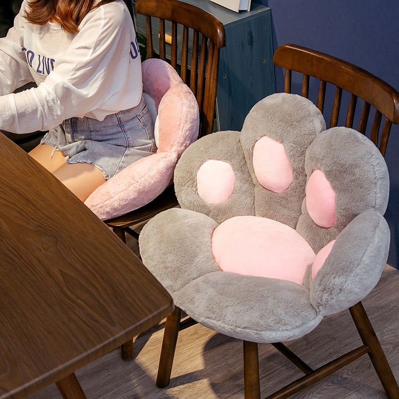 Grey cat paw cushion on chair and a women sitting beside on pink cat paw cushion 