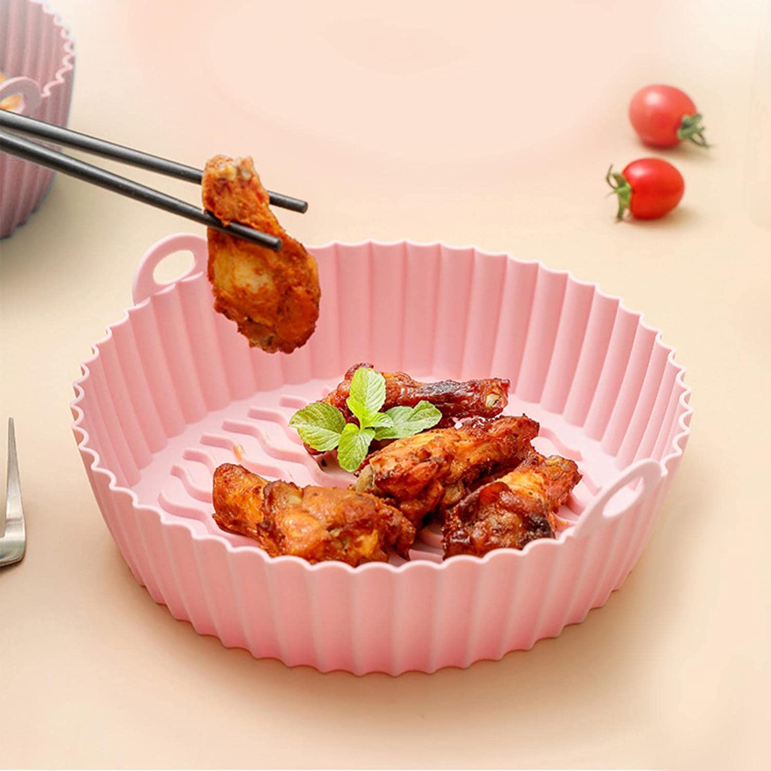 A pair of chopsticks holding pieces of chicken in a pink air fryer basket