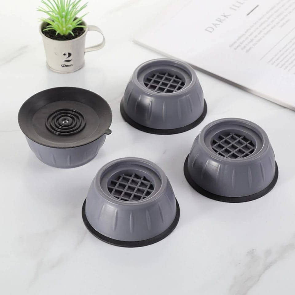 Four Washing Machine Foot Pads with one displaying the underneath side of it placed near to a plant and a magazine 