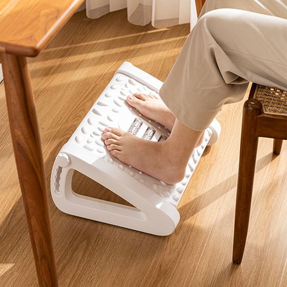 A person sitting comfortably on an adjustable footrest while working on a laptop in a home office setting