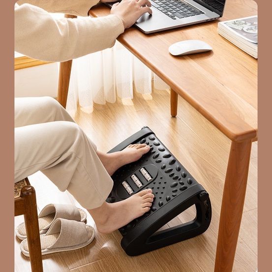 A person sitting comfortably on an adjustable footrest while working on a laptop in a home office setting