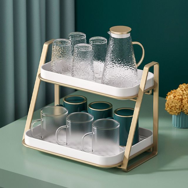 A green table displays a 2 Tier Multifunctional Kitchen Storage Rack holding glasses and cups on its two-tiered tray