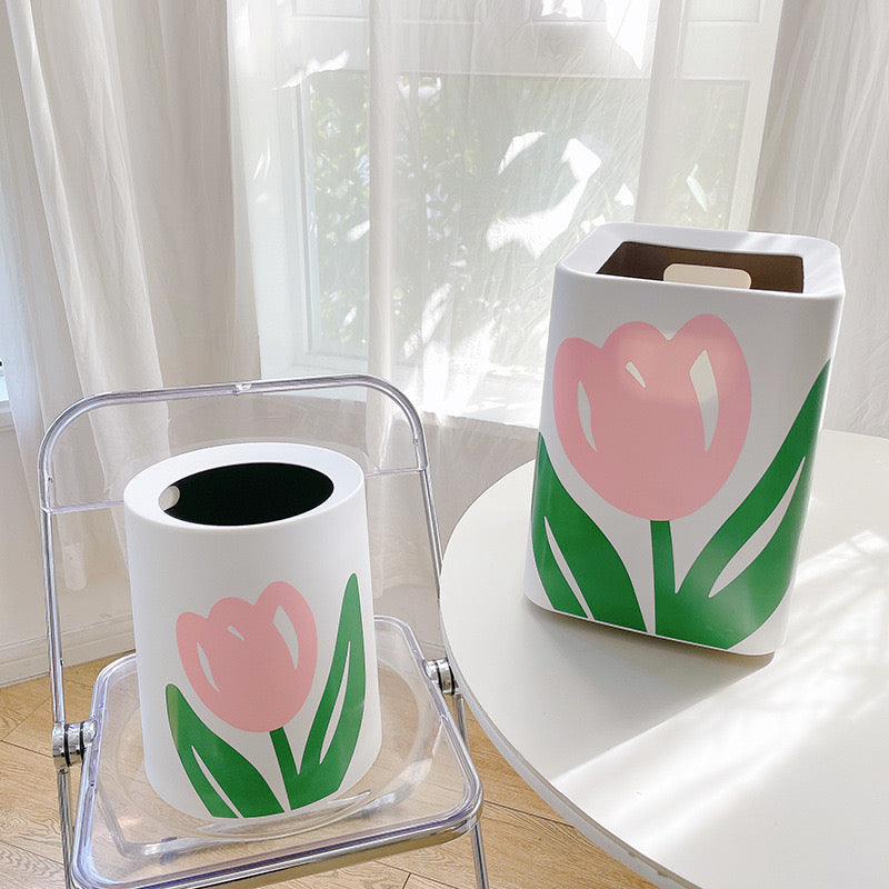 Displaying Flower Design Home Trash Bin in Round and Square shape,Round shaped kept on top of a chair and Square shaped kept on top of a table in a room 